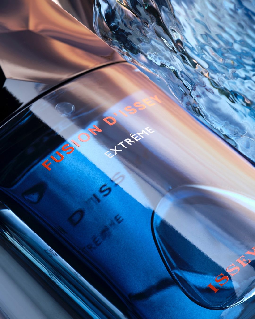 Close-up studio shot of blue perfume bottle with "Fusion D'Issey Extrême" label, water background, and shiny, reflective surfaces.
