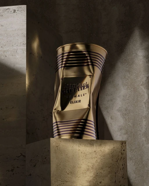 Jean Paul Gaultier 'Le Male Elixir' fragrance can on a stone block. The gold-colored can with dark stripes is slightly crushed.