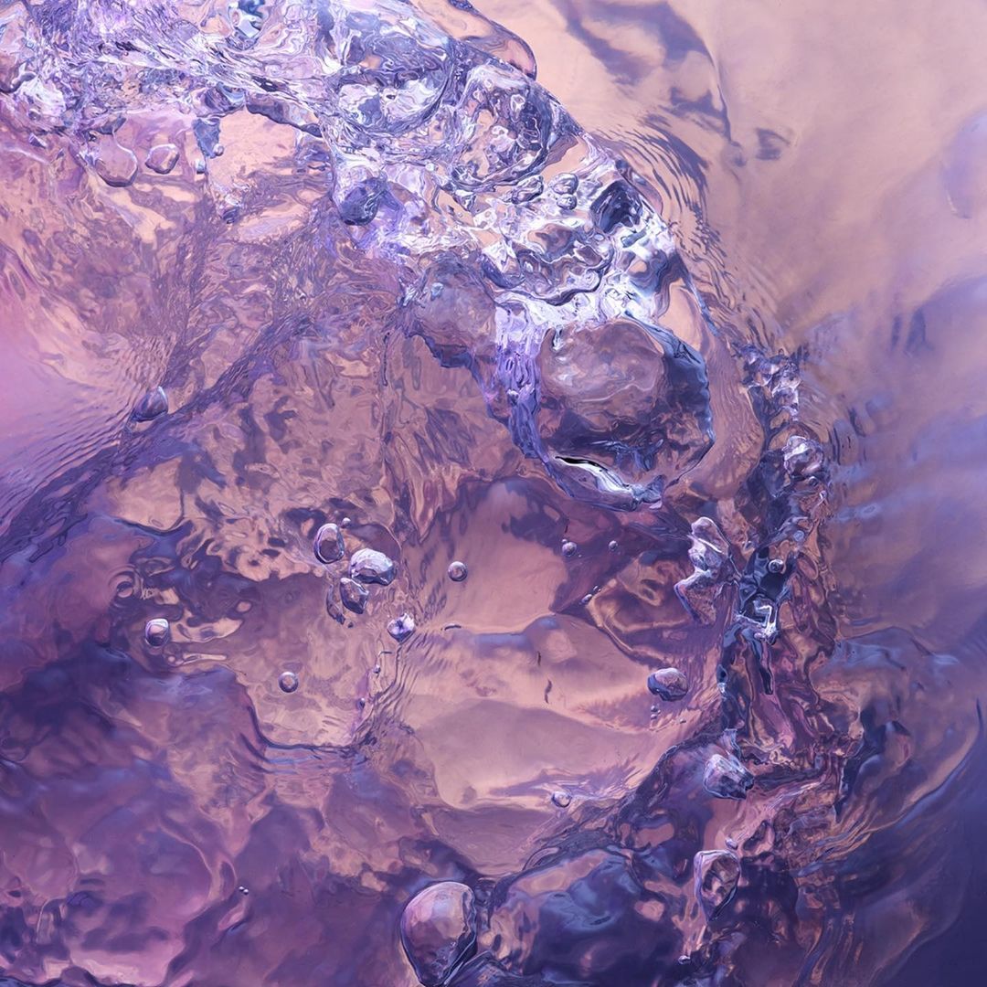 Abstract close-up of flowing water with bubbles and ripples, featuring a purple and pink color palette.