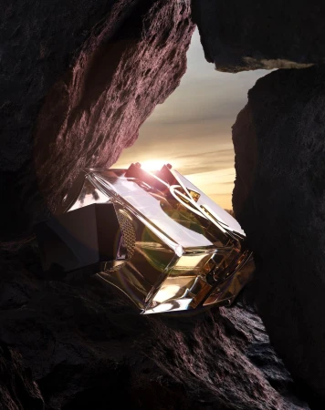 Close-up of a luxury perfume bottle wedged between dark jagged rock formations against a sunset sky.