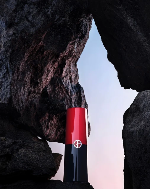 Giorgio Armani lipstick stands between dark rocks against soft gradient background, makeup and beauty, studio product shot for advertising.