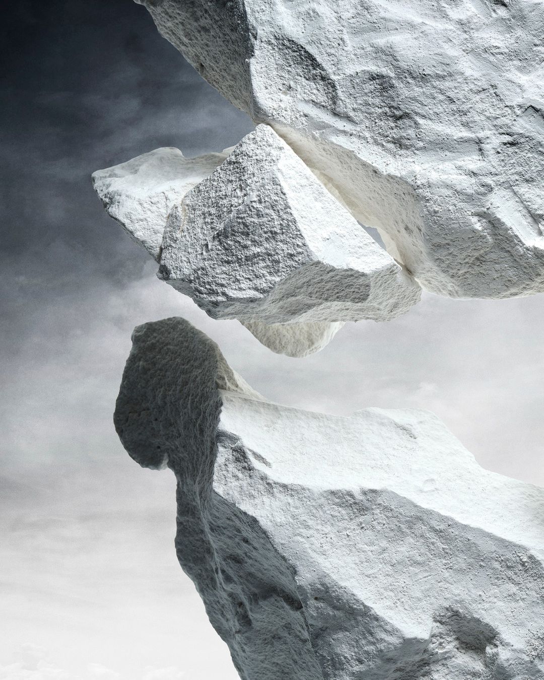 Abstract shot of two large white rocks seemingly suspended in the air against a cloudy sky, creating a surreal, ethereal effect.