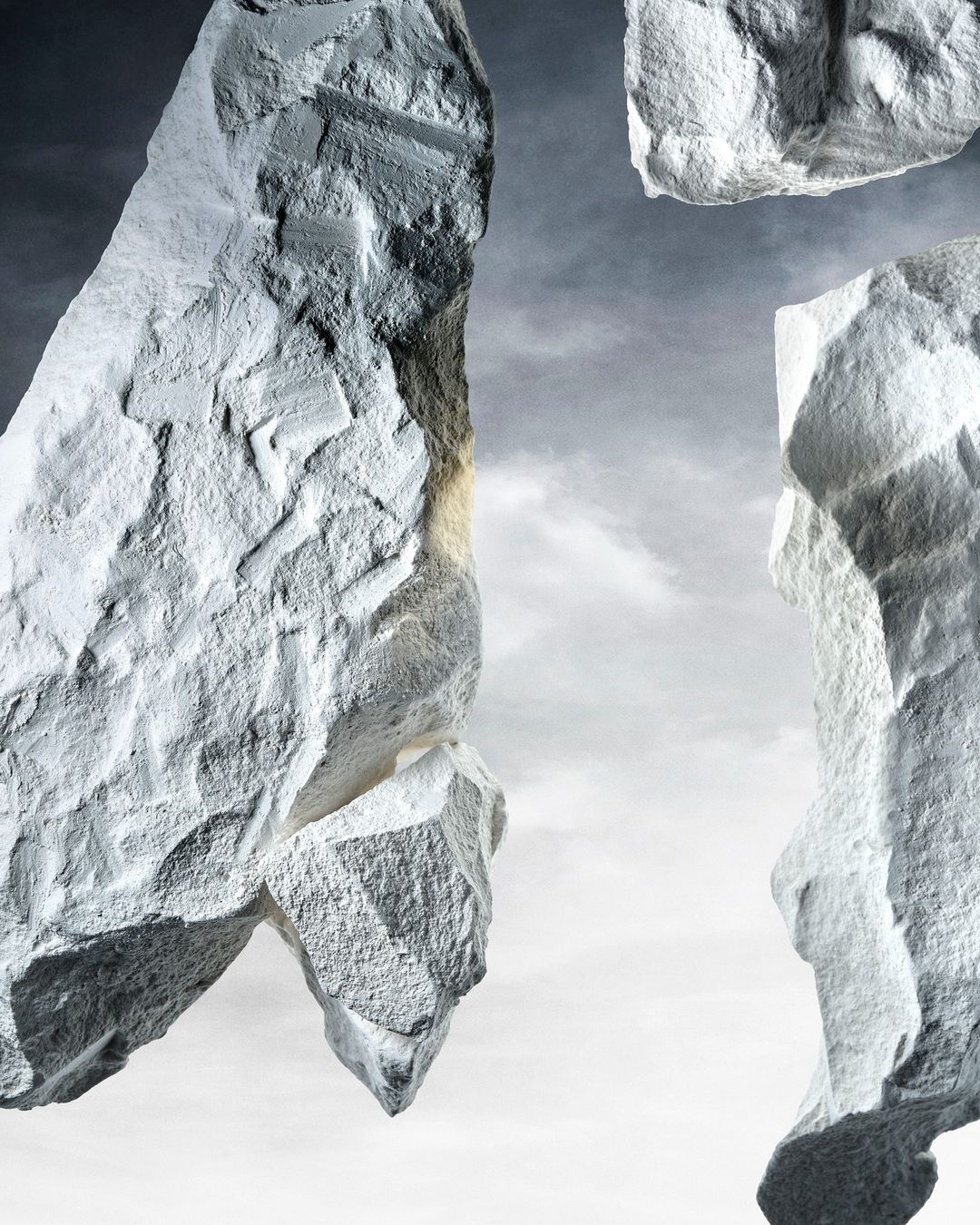 Abstract composition of grey rocks against a light grey sky, featuring rough textures and dramatic lighting with a cloudy backdrop.