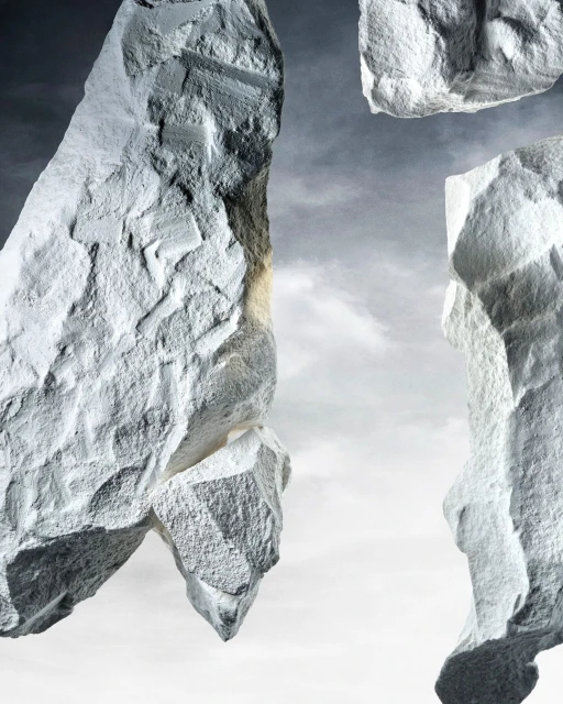 Abstract composition of grey rocks against a light grey sky, featuring rough textures and dramatic lighting with a cloudy backdrop.