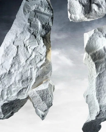 Abstract composition of grey rocks against a light grey sky, featuring rough textures and dramatic lighting with a cloudy backdrop.