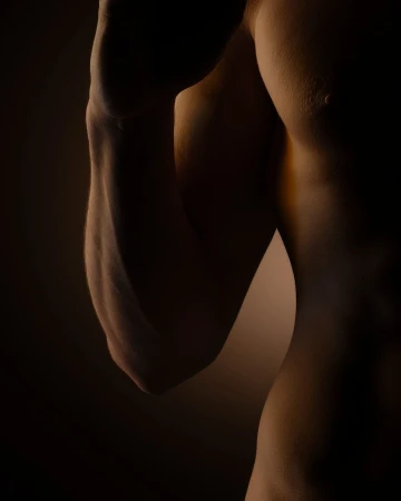 Torso and arm of a muscular adult male are visible against a dark background, highlighting muscle definition and form in a close-up shot.