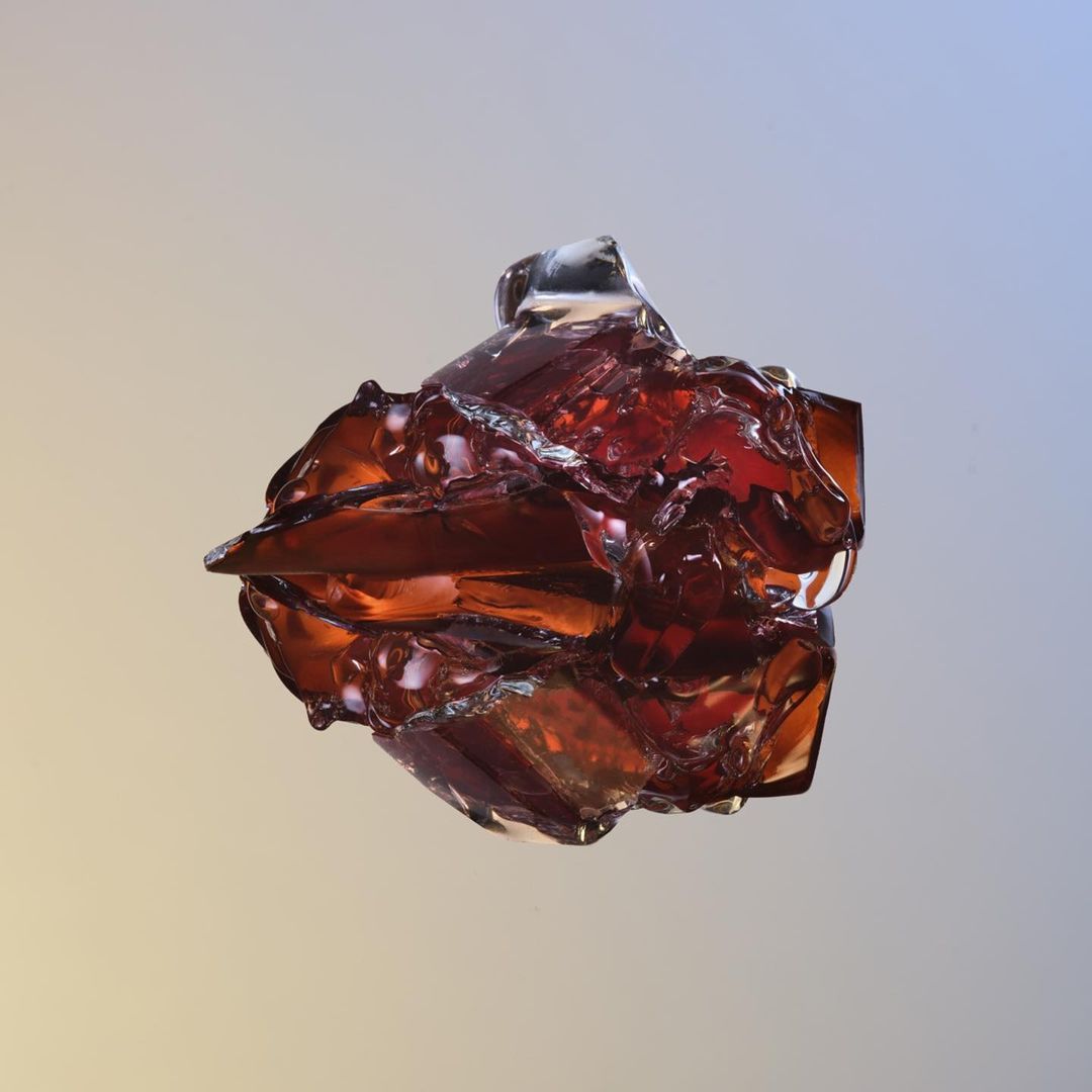 Close-up studio shot of an abstract, crystallized glass object in translucent shades of brown, amber, and clear on a gradient backdrop.