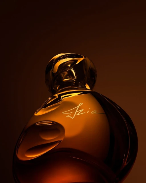 Elegant amber perfume bottle with a curved design and gold lettering, set against a warm brown backdrop for a luxurious beauty product shot.