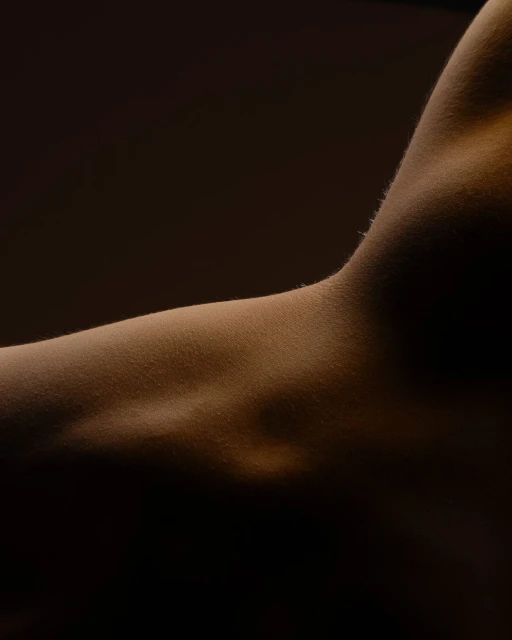Close-up of the upper arm and shoulder of an adult with warm lighting highlighting the skin's texture and subtle shadows.