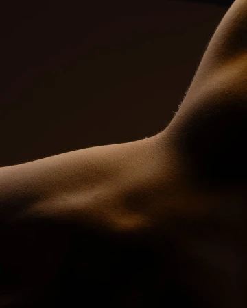 Close-up of the upper arm and shoulder of an adult with warm lighting highlighting the skin's texture and subtle shadows.