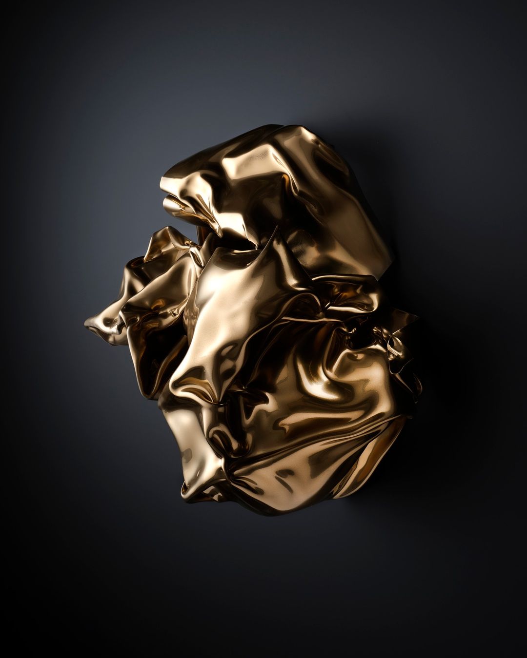 Abstract photo of a gold metallic-colored crumpled fabric sculpture against a dark background, reflecting studio lighting.