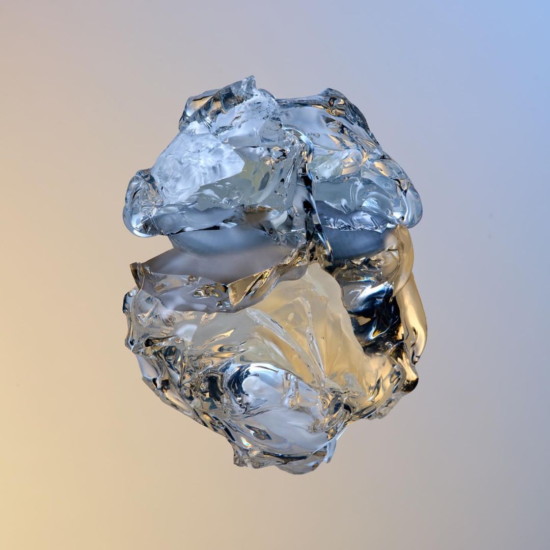 Abstract sculptural form of clear, crystalline material with internal voids, set against a graduated blue to gold background. 