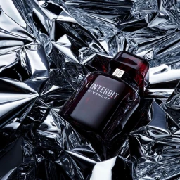 Givenchy L'Interdit perfume bottle resting on a crumpled reflective silver foil background surface.