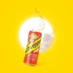 A red Schweppes Agrumes beverage can tilted against a bright yellow background with liquid splashing upward.