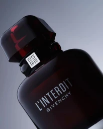 Close-up product shot of a dark red glass perfume bottle with a black cap and silver logo ribbon against a grey background.