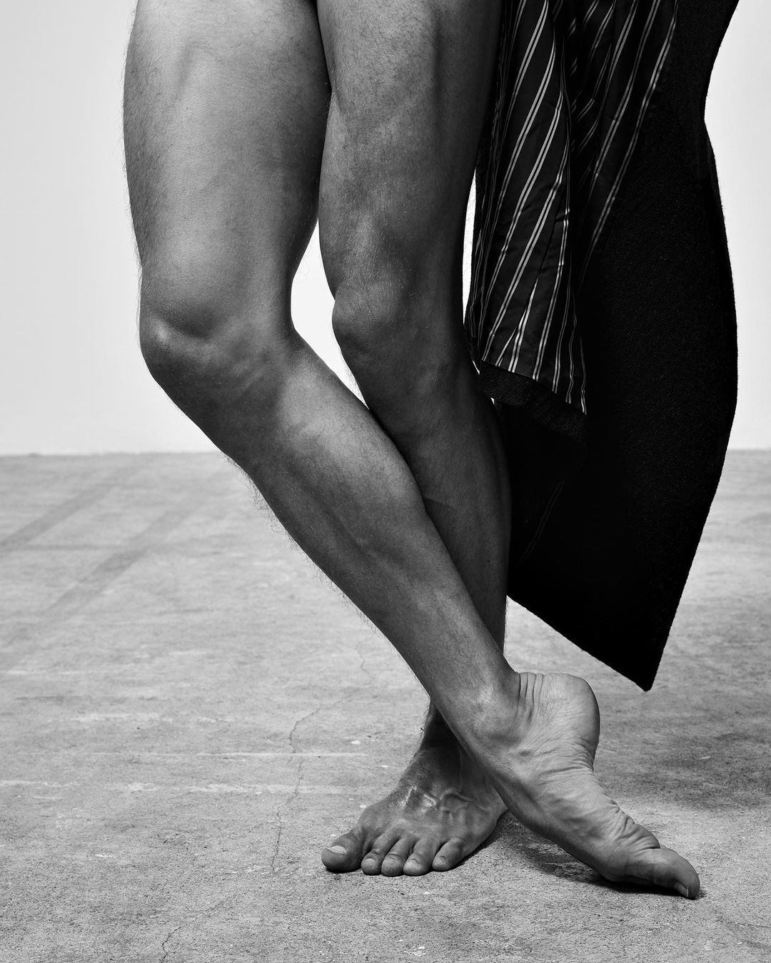 Monochromatic studio image of the lower half of a male adult in a dynamic pose, complemented by a suit jacket draped nearby.