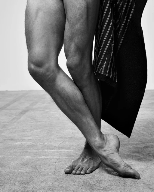 Monochromatic studio image of the lower half of a male adult in a dynamic pose, complemented by a suit jacket draped nearby.