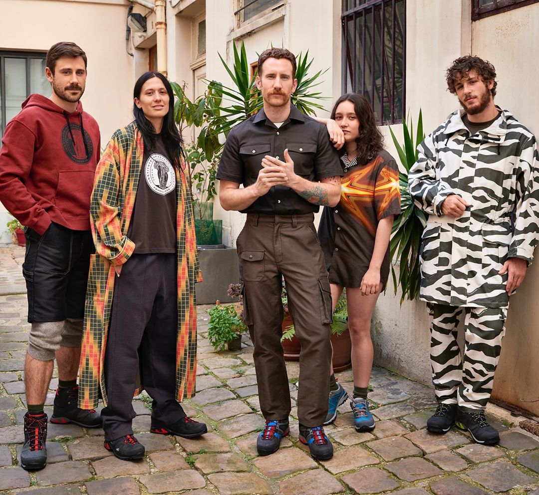 Group portrait of five diverse adults outdoors in casual fashion apparel standing together in an urban courtyard.