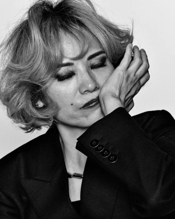 Monochrome portrait of a woman with short blonde hair and dark jacket touching her face with eyes closed, by Christophe Meimoon.