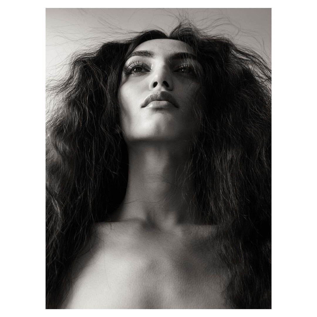 Low-angle monochrome portrait of a woman with dark wavy hair framing her face against a plain background.