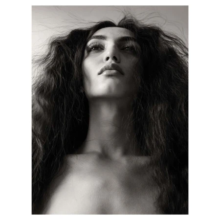 Low-angle monochrome portrait of a woman with dark wavy hair framing her face against a plain background.
