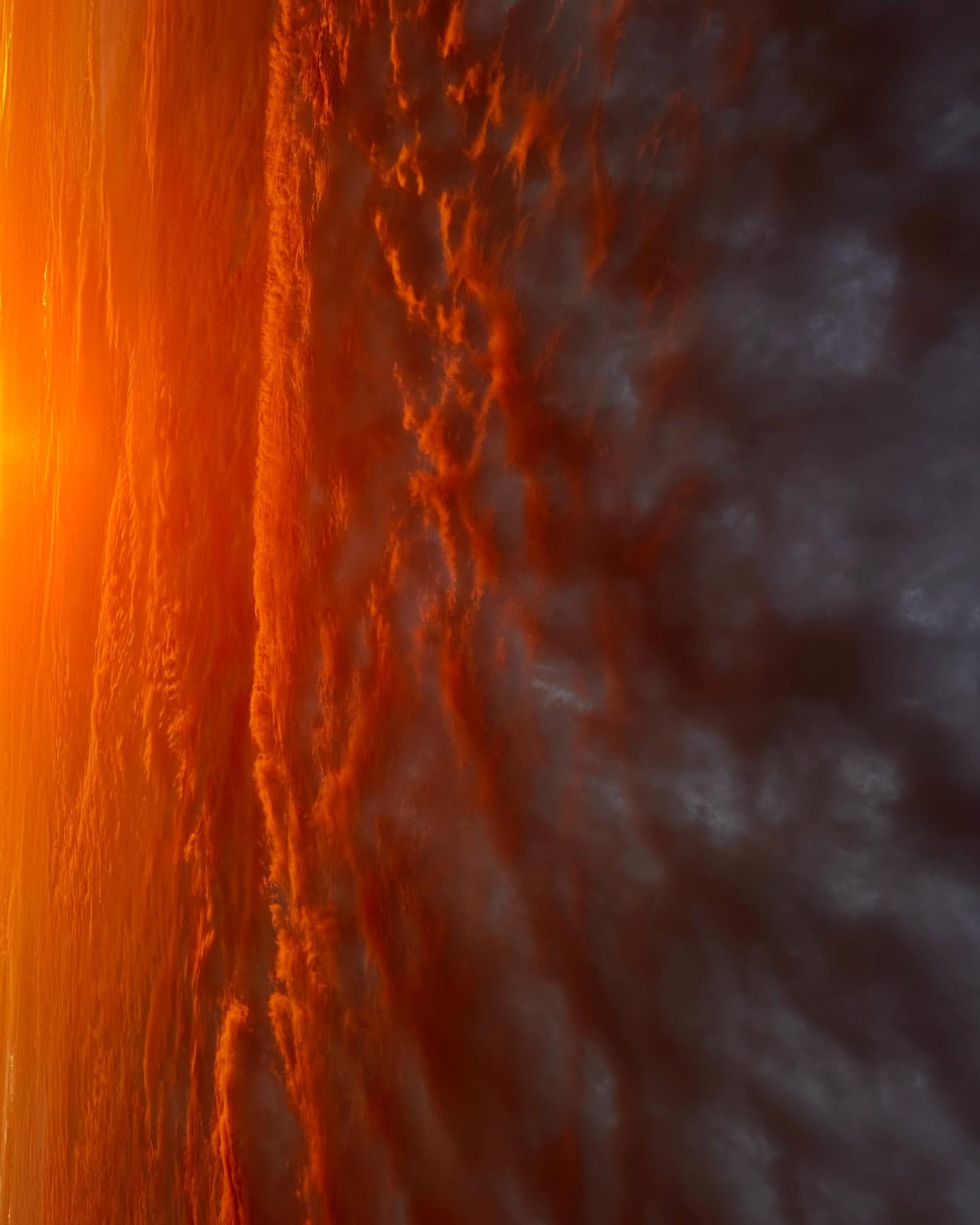 Dramatic cloudscape with orange sunlight breaking through dark storm clouds, creating a textured and visually striking skyscape.