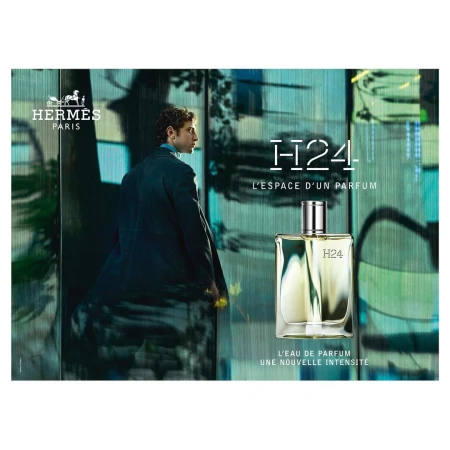 Hermes H24 parfum advertisement featuring a man in a suit standing next to a glass bottle against an abstract blue backdrop.