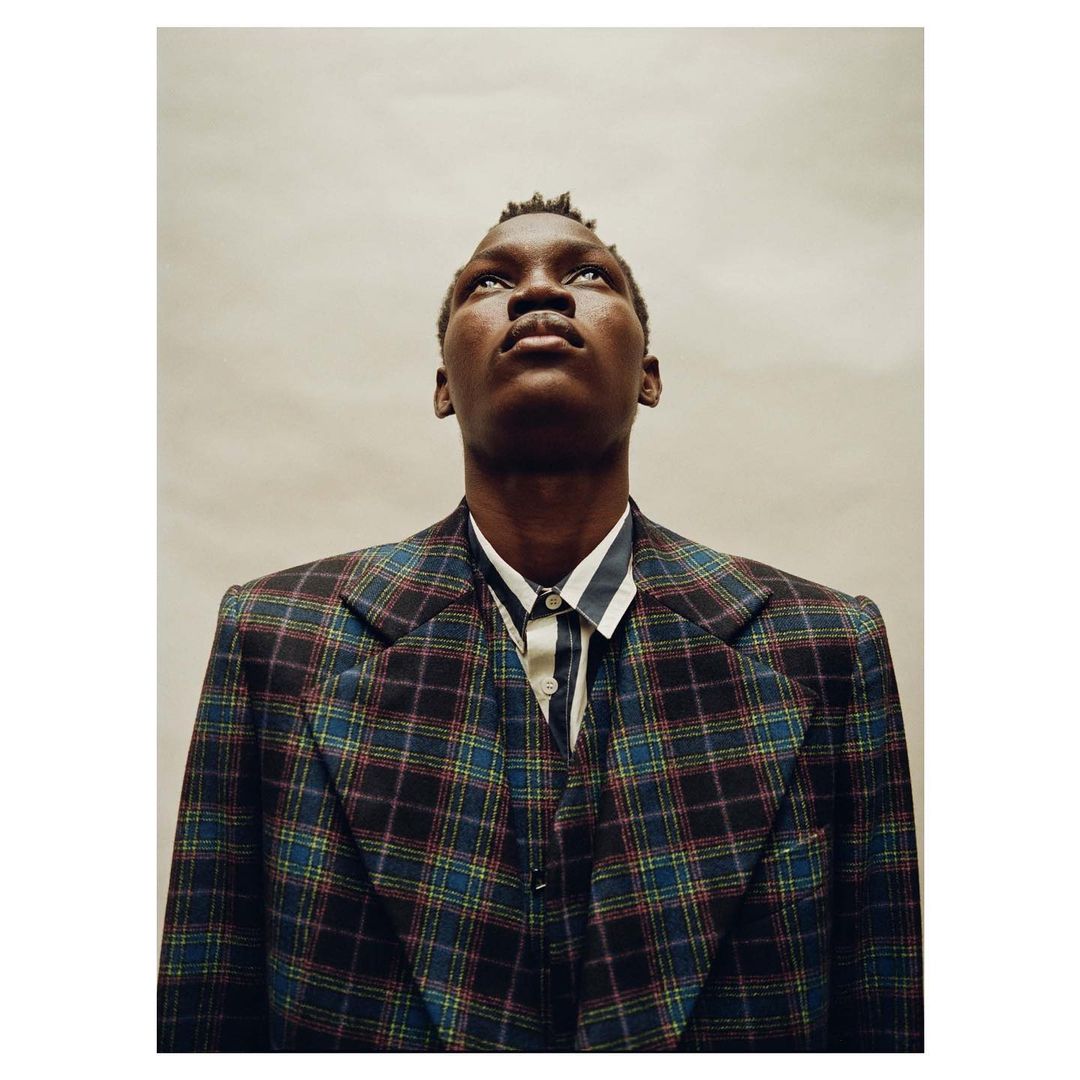 Portrait of Black male in a plaid blazer and striped shirt, looking up against a neutral background, conveying a sense of introspection.