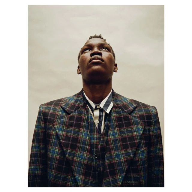 Portrait of Black male in a plaid blazer and striped shirt, looking up against a neutral background, conveying a sense of introspection.