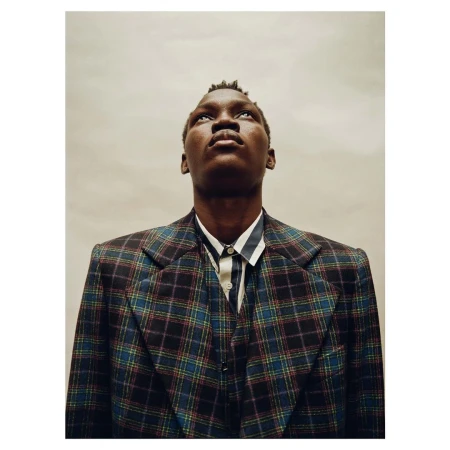 Portrait of Black male in a plaid blazer and striped shirt, looking up against a neutral background, conveying a sense of introspection.