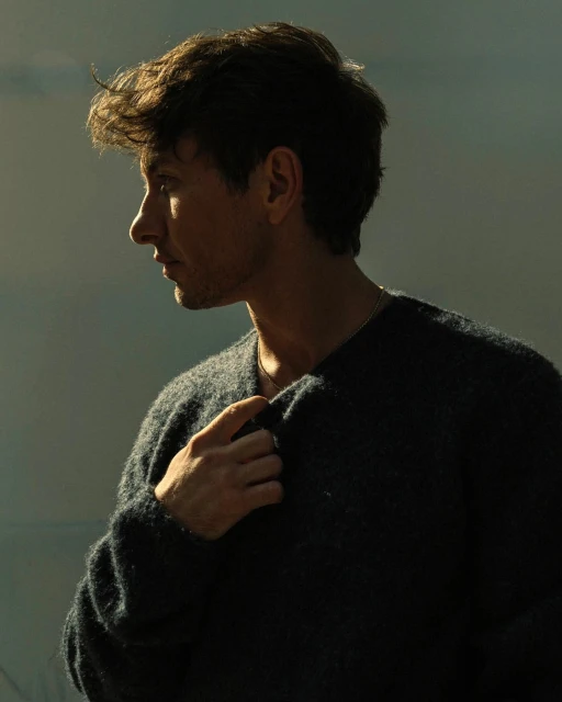 Portrait of a handsome man in a dark sweater, side profile with blurred background, warm lighting, and shallow depth of field. 