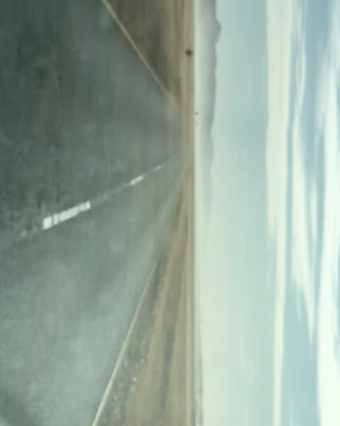 Eye-level shot of empty asphalt road stretching toward distant mountains, under a cloudy sky. Gray asphalt dominant.
