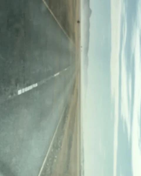 Eye-level shot of empty asphalt road stretching toward distant mountains, under a cloudy sky. Gray asphalt dominant.