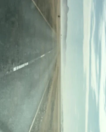 Eye-level shot of empty asphalt road stretching toward distant mountains, under a cloudy sky. Gray asphalt dominant.