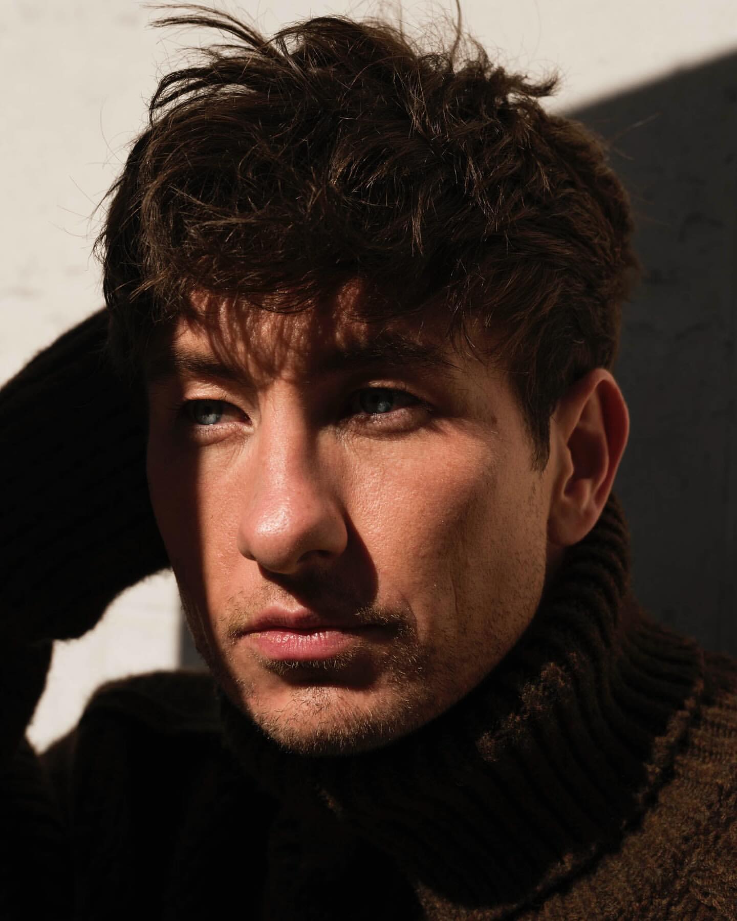 Close-up portrait of actor Barry Keoghan wearing a dark ribbed turtleneck sweater in bright sunlight with harsh shadows.
