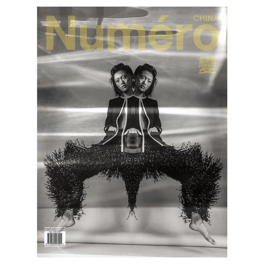 Fashion magazine cover featuring a symmetrical photo of an Asian female model wearing an outfit with fringe, shot in black and white.