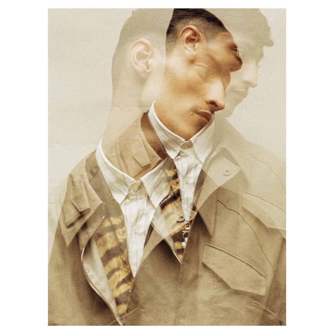 Fashionable man with multiple exposures wearing a beige jacket and striped shirt, posing in a photo studio with warm-toned lighting.