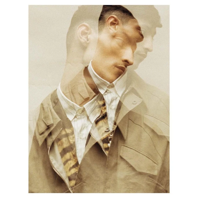 Fashionable man with multiple exposures wearing a beige jacket and striped shirt, posing in a photo studio with warm-toned lighting.