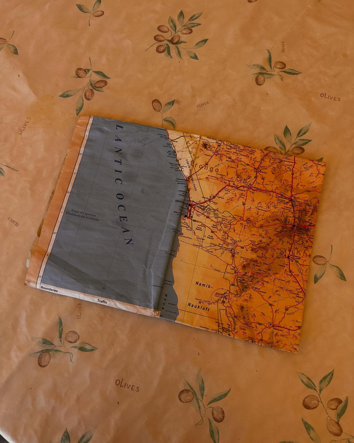 Open world map on an olive-patterned tablecloth, displaying orange landmasses and a blue ocean labeled 'Atlantic Ocean'.