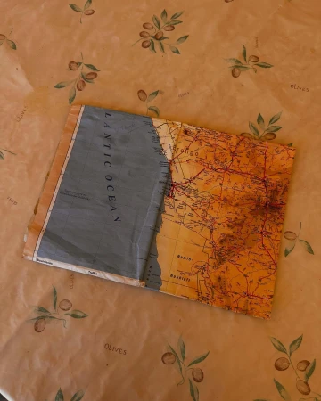 Open world map on an olive-patterned tablecloth, displaying orange landmasses and a blue ocean labeled 'Atlantic Ocean'.