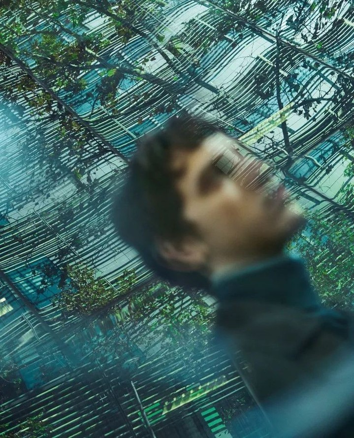 Abstract portrait of a blurry man in a dark jacket, with a background of greenery and geometric lines, creating an artistic and distorted effect.