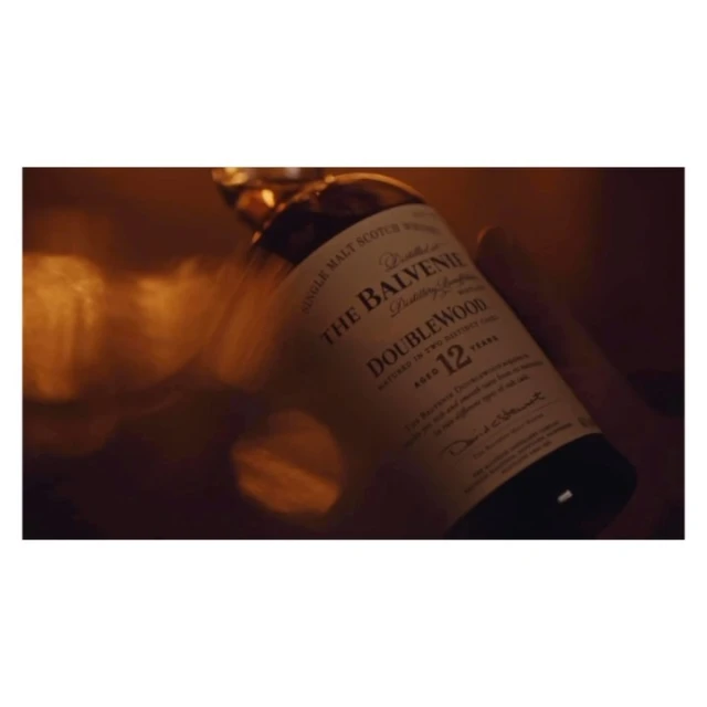 The Balvenie Doublewood 12-year single malt Scotch whisky bottle with dark green cap and blurred golden background in soft focus.