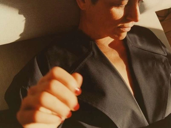 Close-up portrait of a person in a dark coat with sunlight casting sharp shadows across the face and hand.