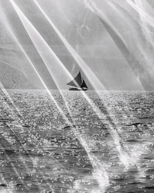 Black and white photograph of a sailboat on calm open water, light streaks across the frame, creating a vintage or artistic aesthetic.