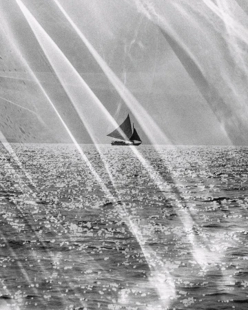 Black and white photograph of a sailboat on calm open water, light streaks across the frame, creating a vintage or artistic aesthetic.