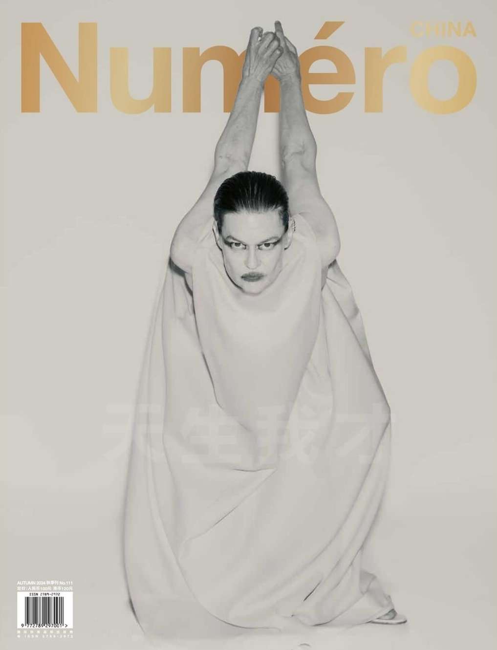 Fashion magazine cover featuring a model in a light-colored gown with hands raised, against a white background with gold lettering.
