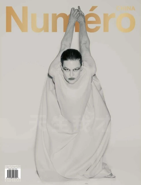 Fashion magazine cover featuring a model in a light-colored gown with hands raised, against a white background with gold lettering.