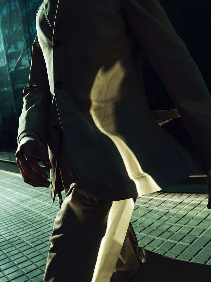 Man in suit walks on textured metal walkway. Strong directional light creating bold shadows on the figure and ground in an urban setting.