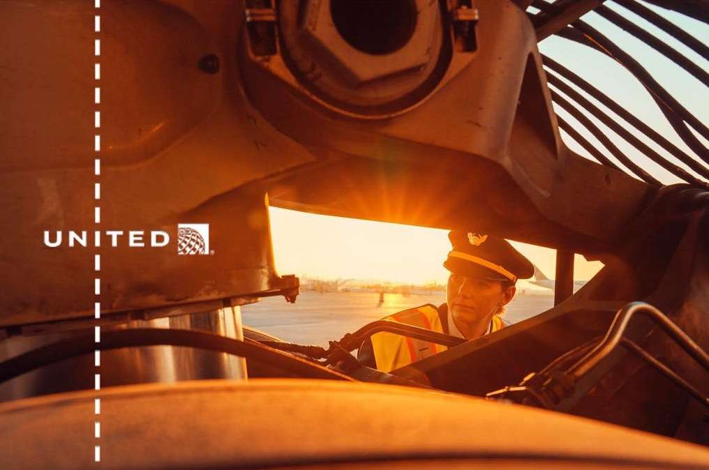 Adult male pilot in uniform stands next to a commercial airplane on an airport runway during golden hour, with visible United logo.