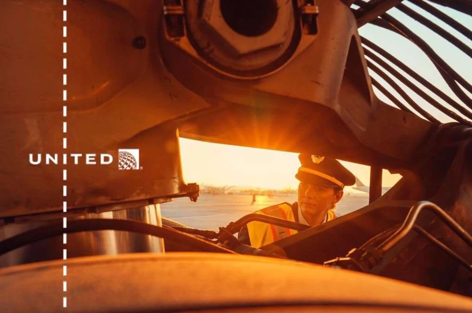 Adult male pilot in uniform stands next to a commercial airplane on an airport runway during golden hour, with visible United logo.